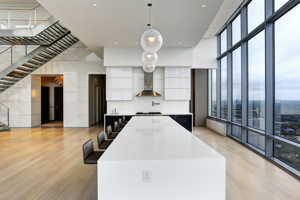 Large contemporary open plan kitchen in Houston with a submerged sink, flat-panel cabinets, white cabinets, quartz worktops, white splashback, stainless steel appliances, light hardwood flooring and an island.