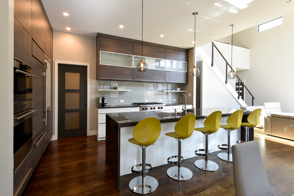 Foto di una cucina minimal con ante lisce, ante in legno bruno, paraspruzzi grigio, paraspruzzi con piastrelle di vetro, elettrodomestici neri e parquet scuro