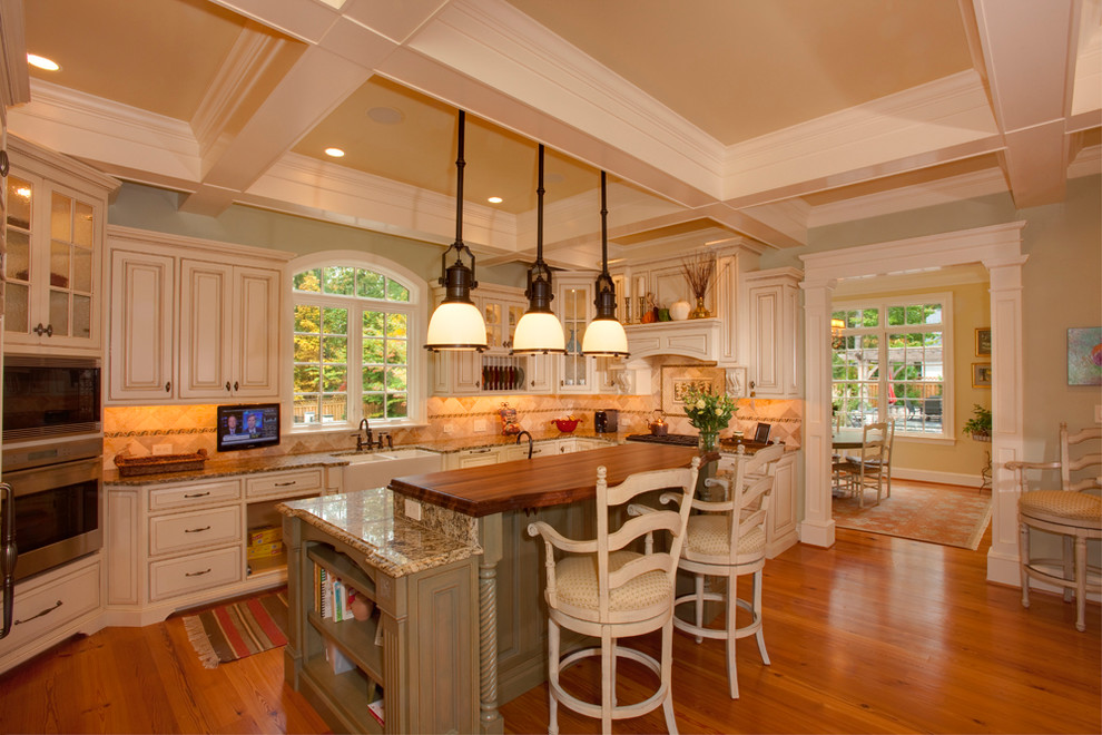 Exempel på ett avskilt, stort klassiskt l-kök, med en rustik diskho, luckor med infälld panel, vita skåp, granitbänkskiva, beige stänkskydd, stänkskydd i keramik, vita vitvaror, ljust trägolv och en köksö