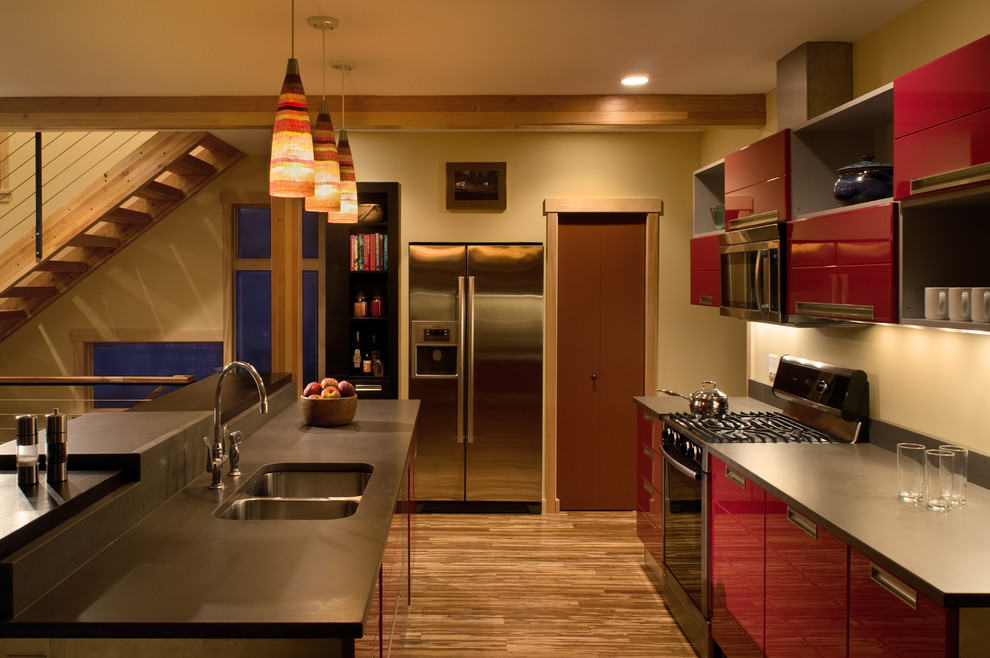 Diseño de cocina comedor contemporánea grande con fregadero bajoencimera, puertas de armario rojas, electrodomésticos de acero inoxidable, suelo de madera clara y una isla