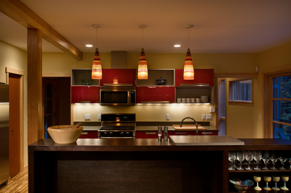Modelo de cocina comedor actual grande con fregadero bajoencimera, puertas de armario rojas, electrodomésticos de acero inoxidable, suelo de madera clara y una isla