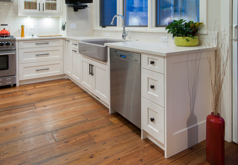 Example of a beach style dark wood floor and brown floor kitchen design in Calgary with a farmhouse sink, shaker cabinets, white cabinets, quartzite countertops, white backsplash, subway tile backsplash and stainless steel appliances