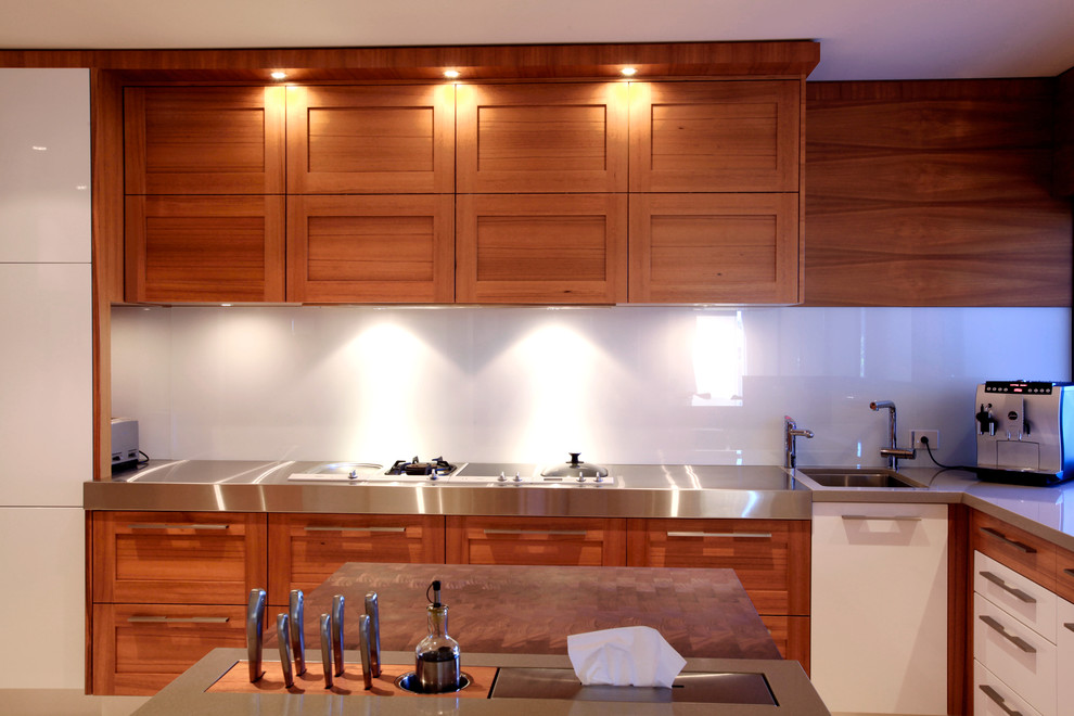 Exempel på ett 60 tals kök, med en undermonterad diskho, skåp i shakerstil, skåp i mellenmörkt trä, vitt stänkskydd, glaspanel som stänkskydd och en köksö