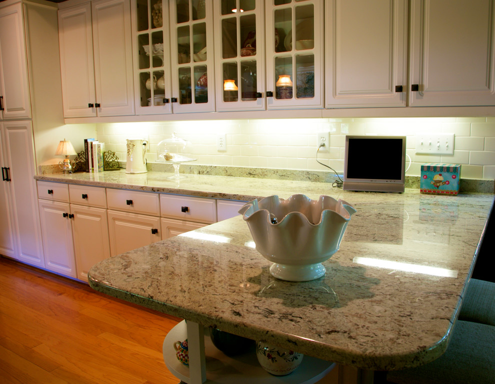 Inredning av ett klassiskt mellanstort kök, med luckor med upphöjd panel, vita skåp, granitbänkskiva, vitt stänkskydd, fönster som stänkskydd, mellanmörkt trägolv, en halv köksö och brunt golv