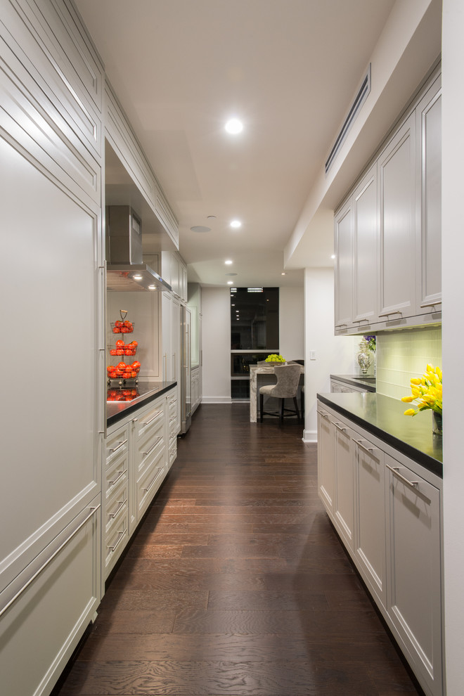 Example of a large trendy galley dark wood floor enclosed kitchen design in Houston with an undermount sink, recessed-panel cabinets, white cabinets, granite countertops, white backsplash, ceramic backsplash, paneled appliances and no island
