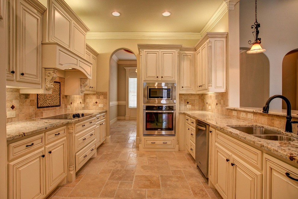 Example of a mid-sized classic galley ceramic tile and beige floor open concept kitchen design in Dallas with an undermount sink, raised-panel cabinets, white cabinets, granite countertops, beige backsplash, ceramic backsplash, stainless steel appliances and a peninsula