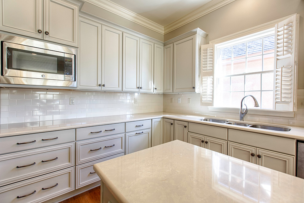 Inspiration for a mid-sized timeless u-shaped light wood floor eat-in kitchen remodel in Birmingham with a triple-bowl sink, flat-panel cabinets, gray cabinets, quartz countertops, white backsplash, subway tile backsplash, stainless steel appliances and an island