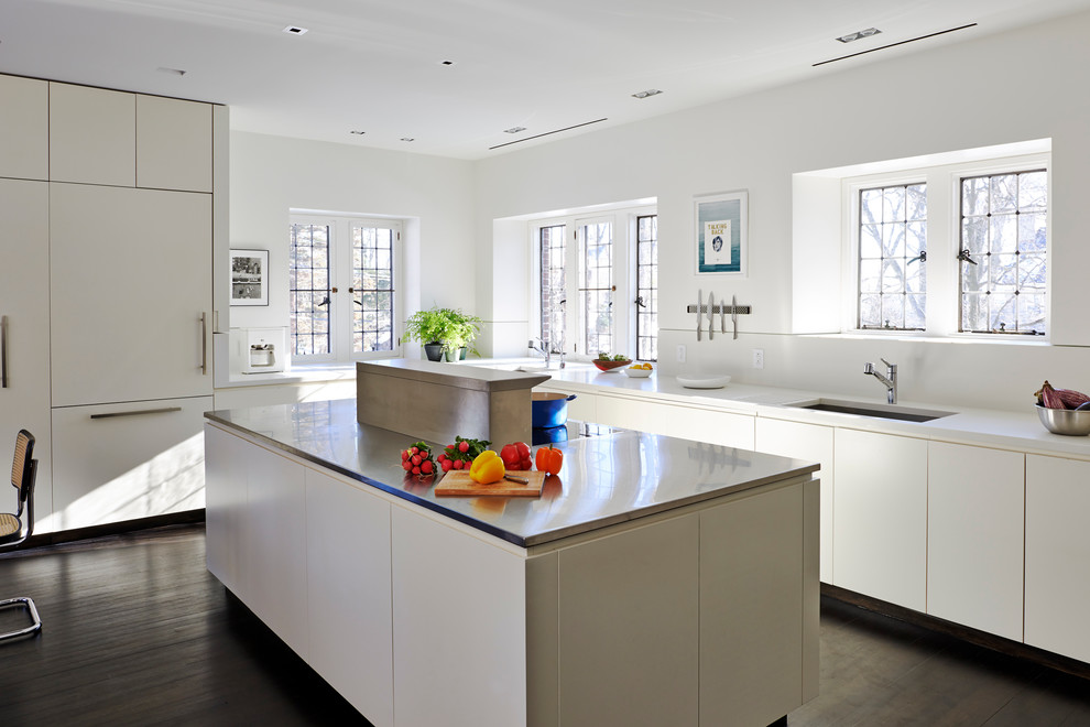 На фото: угловая кухня в современном стиле с врезной мойкой, плоскими фасадами, белыми фасадами, белым фартуком, темным паркетным полом, островом и окном