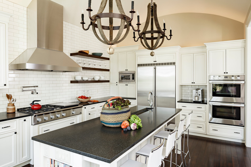 Example of a large trendy u-shaped dark wood floor and brown floor kitchen design in Portland with white cabinets, white backsplash, subway tile backsplash, stainless steel appliances, an undermount sink, recessed-panel cabinets, granite countertops and an island