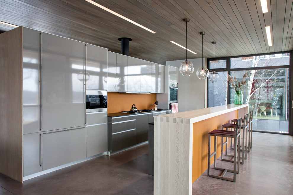Стильный дизайн: параллельная, глянцевая кухня в современном стиле с плоскими фасадами, серыми фасадами, оранжевым фартуком и техникой под мебельный фасад - последний тренд