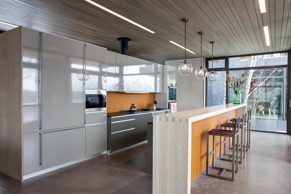 Inspiration for a contemporary galley kitchen remodel in New York with flat-panel cabinets, gray cabinets, orange backsplash and paneled appliances