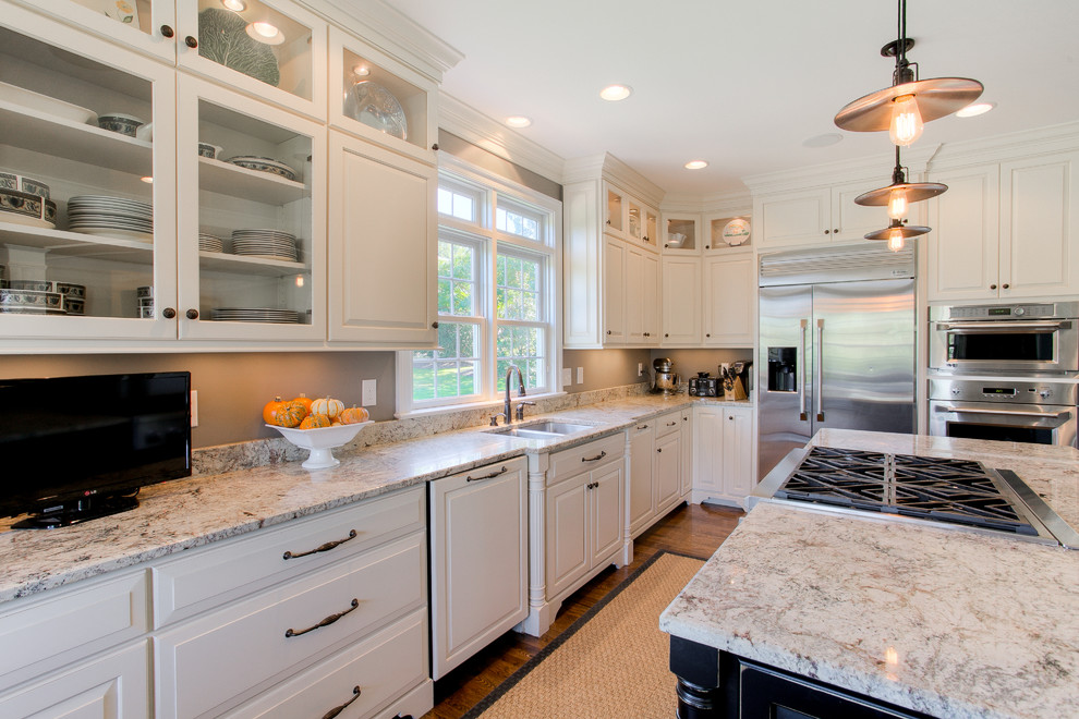 Klassisk inredning av ett mellanstort kök, med en dubbel diskho, luckor med upphöjd panel, vita skåp, granitbänkskiva, rostfria vitvaror, mörkt trägolv, en köksö och brunt golv