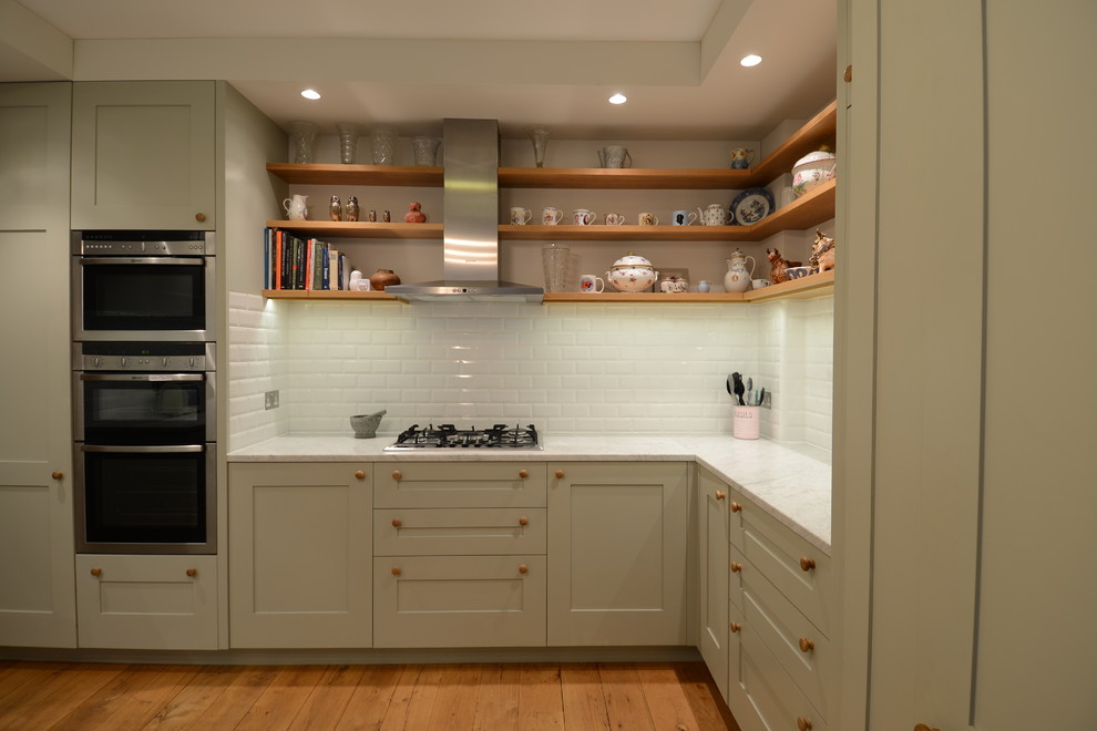 Inspiration for a small scandinavian u-shaped enclosed kitchen in London with an integrated sink, shaker cabinets, green cabinets, marble worktops, white splashback, metro tiled splashback, stainless steel appliances, light hardwood flooring and no island.