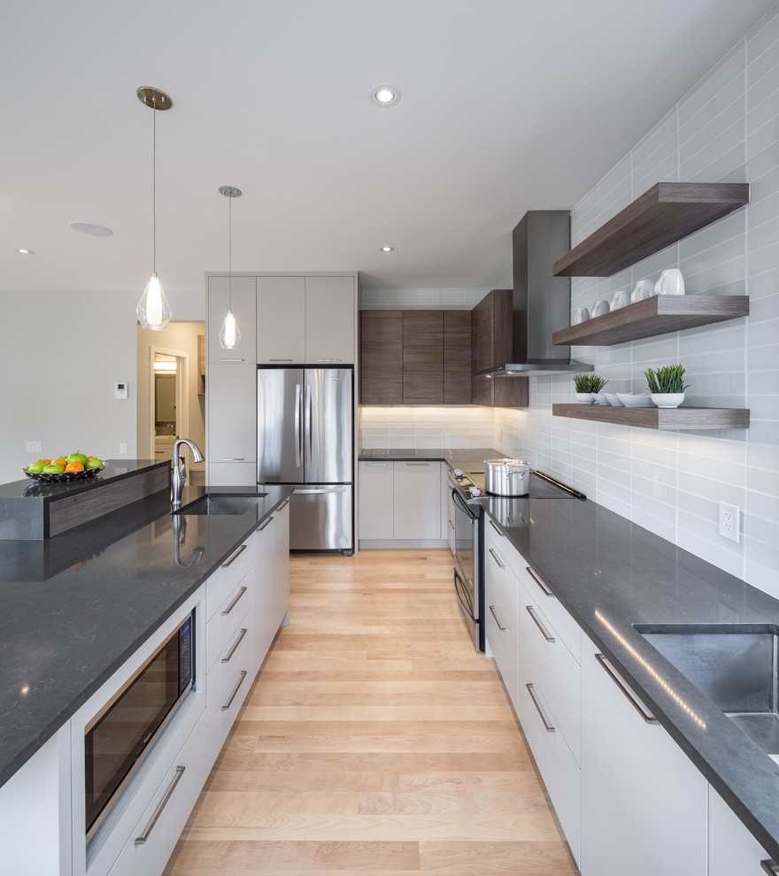 Moderne Küche mit Unterbauwaschbecken, flächenbündigen Schrankfronten, grauen Schränken, Küchenrückwand in Grau, Küchengeräten aus Edelstahl, hellem Holzboden und Kücheninsel in Toronto