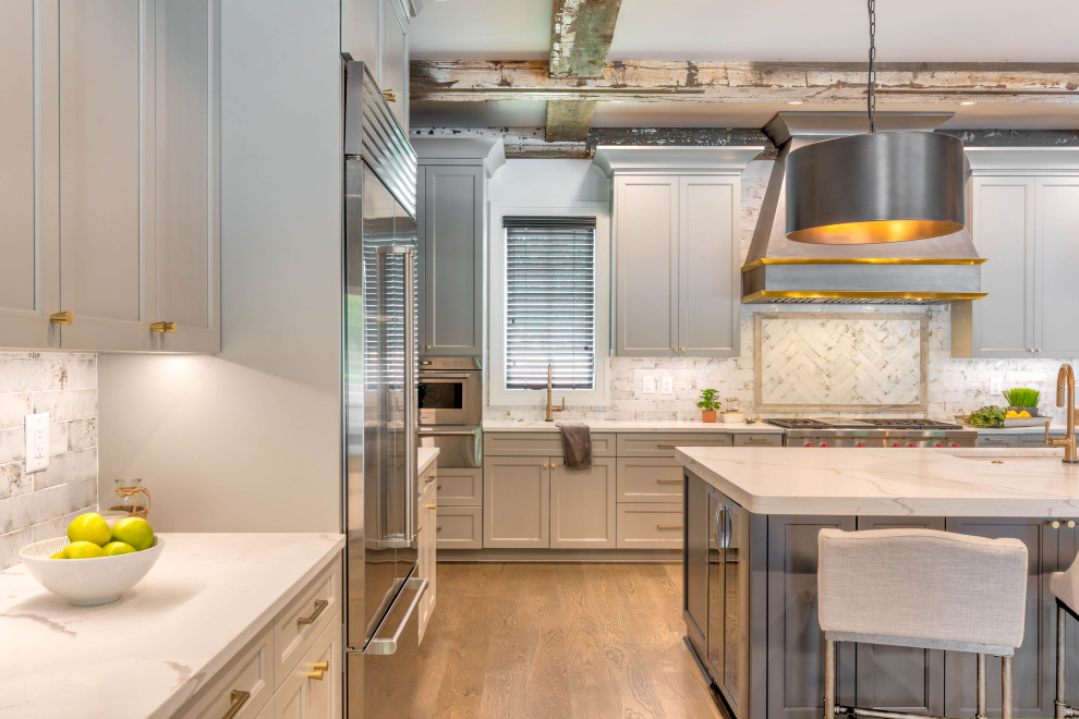 Expansive traditional l-shaped kitchen/diner in Atlanta with a submerged sink, shaker cabinets, grey cabinets, engineered stone countertops, white splashback, ceramic splashback, stainless steel appliances, medium hardwood flooring, an island, brown floors, white worktops and exposed beams.