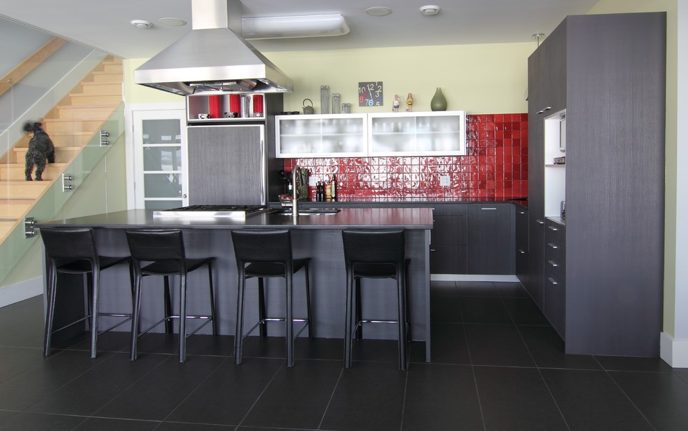 Cette image montre une cuisine minimaliste en L avec un placard à porte plane, des portes de placard noires, une crédence rouge et un sol noir.