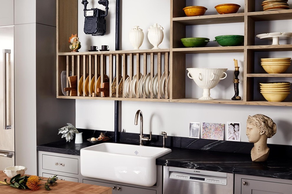 Example of a mid-sized transitional l-shaped concrete floor enclosed kitchen design in New York with a farmhouse sink, shaker cabinets, gray cabinets, soapstone countertops, black backsplash, stone slab backsplash, stainless steel appliances and an island