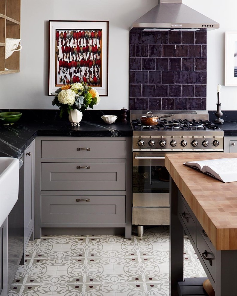 Enclosed kitchen - mid-sized transitional l-shaped enclosed kitchen idea in New York with a farmhouse sink, shaker cabinets, gray cabinets, soapstone countertops, black backsplash, stainless steel appliances, an island and stone tile backsplash