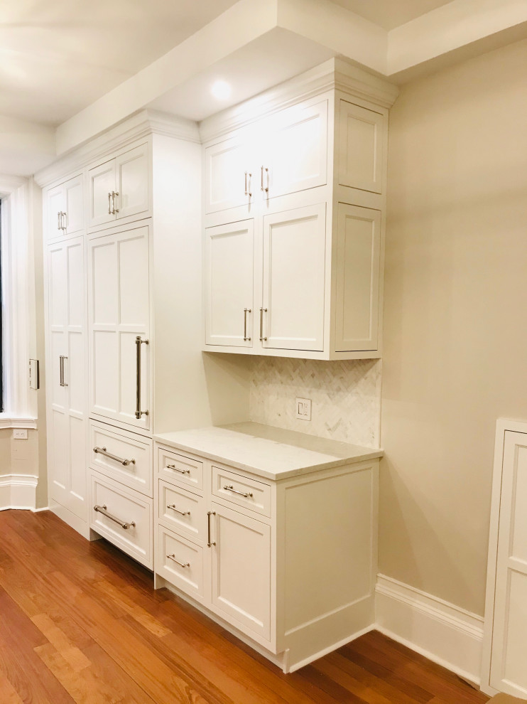Inredning av ett klassiskt litet vit vitt kök, med en undermonterad diskho, luckor med infälld panel, vita skåp, bänkskiva i kvarts, flerfärgad stänkskydd, stänkskydd i marmor, integrerade vitvaror, mörkt trägolv och brunt golv