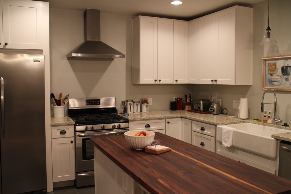 Inredning av ett lantligt mellanstort kök, med en rustik diskho, luckor med infälld panel, vita skåp, träbänkskiva, grått stänkskydd, rostfria vitvaror, klinkergolv i porslin och en köksö