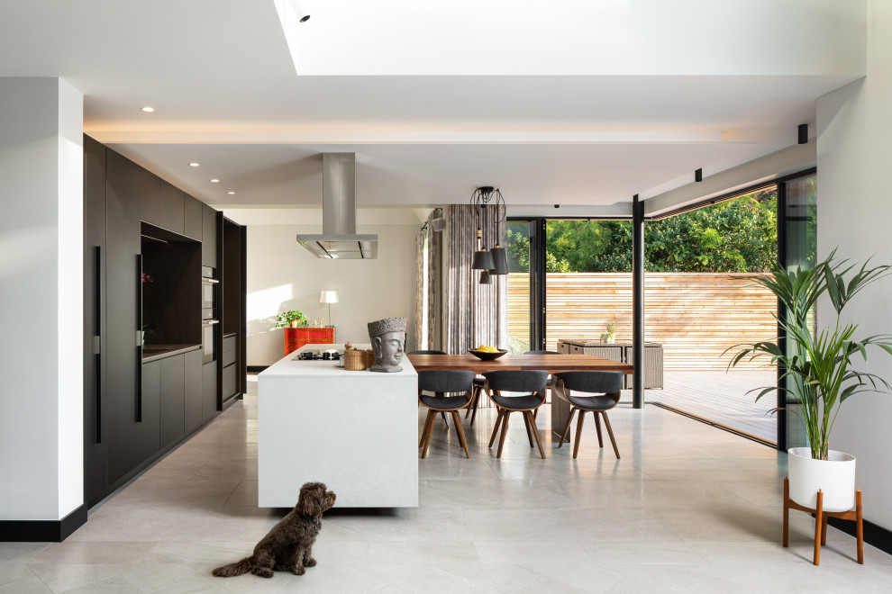Offene, Zweizeilige Moderne Küche mit flächenbündigen Schrankfronten, schwarzen Schränken, schwarzen Elektrogeräten, Kücheninsel, grauem Boden und weißer Arbeitsplatte in Surrey