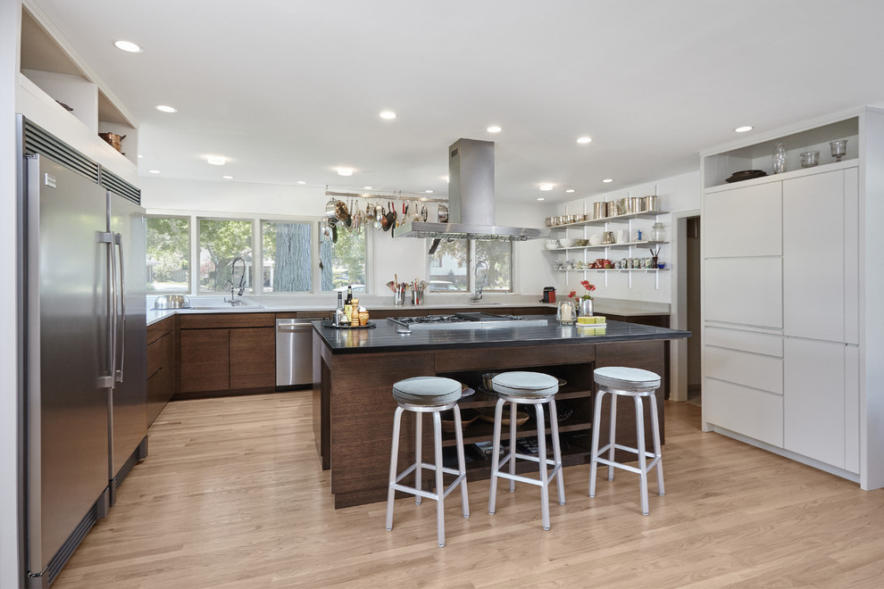 Immagine di una cucina contemporanea con ante lisce, ante in legno bruno, elettrodomestici in acciaio inossidabile, parquet chiaro, pavimento beige e top nero