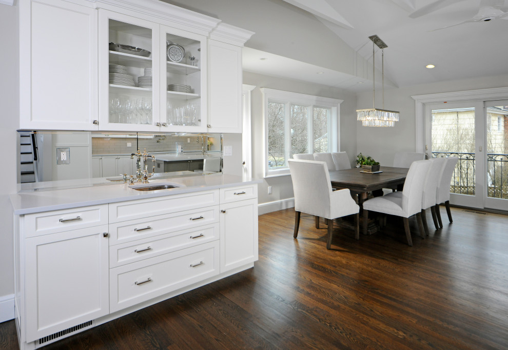 Exempel på ett mellanstort klassiskt vit vitt kök, med en dubbel diskho, släta luckor, vita skåp, bänkskiva i kvarts, beige stänkskydd, stänkskydd i glaskakel, rostfria vitvaror, mörkt trägolv, en köksö och brunt golv