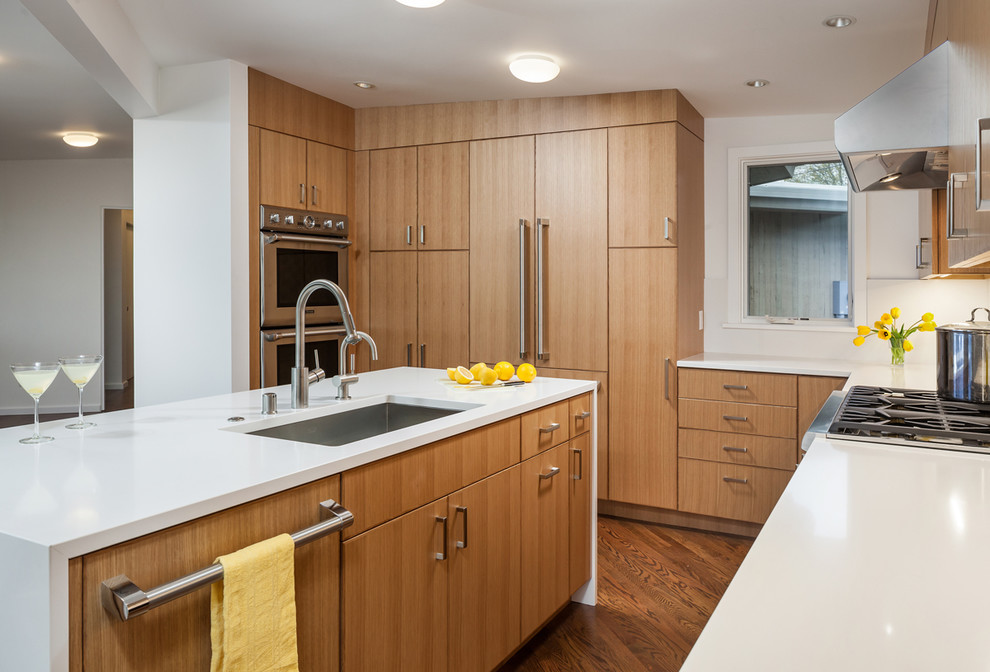 Bild på ett avskilt, stort funkis vit vitt u-kök, med en köksö, en undermonterad diskho, släta luckor, skåp i mellenmörkt trä, bänkskiva i kvarts, vitt stänkskydd, integrerade vitvaror, mörkt trägolv och brunt golv