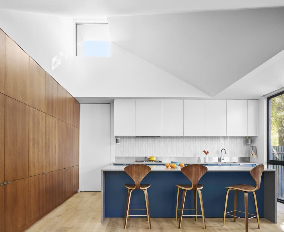 Moderne Küche mit Kücheninsel, flächenbündigen Schrankfronten, weißen Schränken, Küchenrückwand in Weiß, hellem Holzboden und grauer Arbeitsplatte in Austin