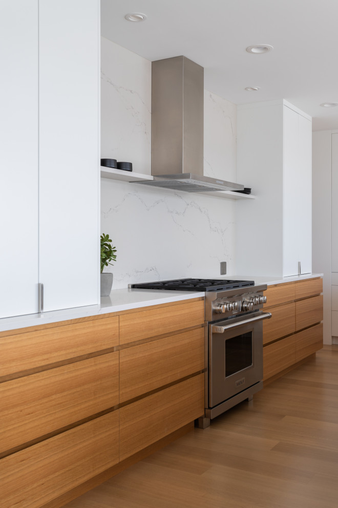 Bild på ett stort funkis vit vitt kök och matrum, med en undermonterad diskho, släta luckor, skåp i ljust trä, bänkskiva i kvarts, vitt stänkskydd, stänkskydd i sten, rostfria vitvaror, ljust trägolv och en köksö