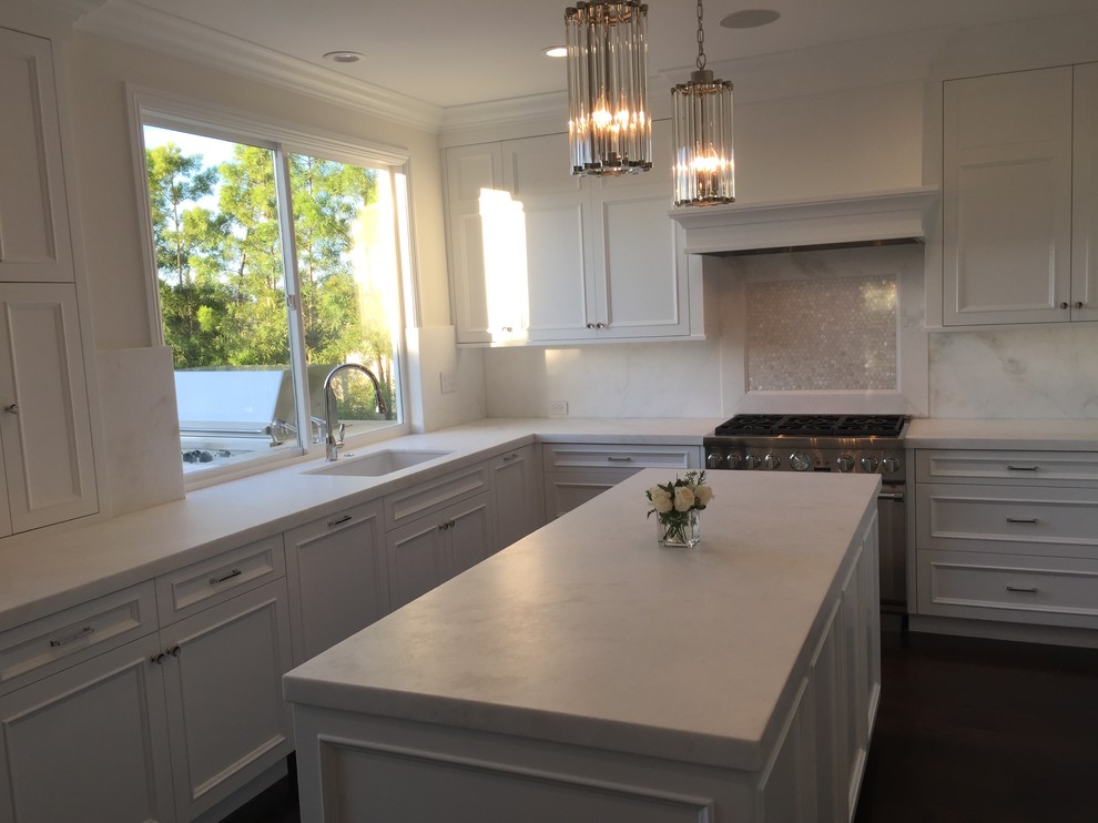 Photo of a medium sized traditional u-shaped enclosed kitchen in Orange County with a built-in sink, beaded cabinets, white cabinets, marble worktops, white splashback, marble splashback, white appliances, dark hardwood flooring and an island.