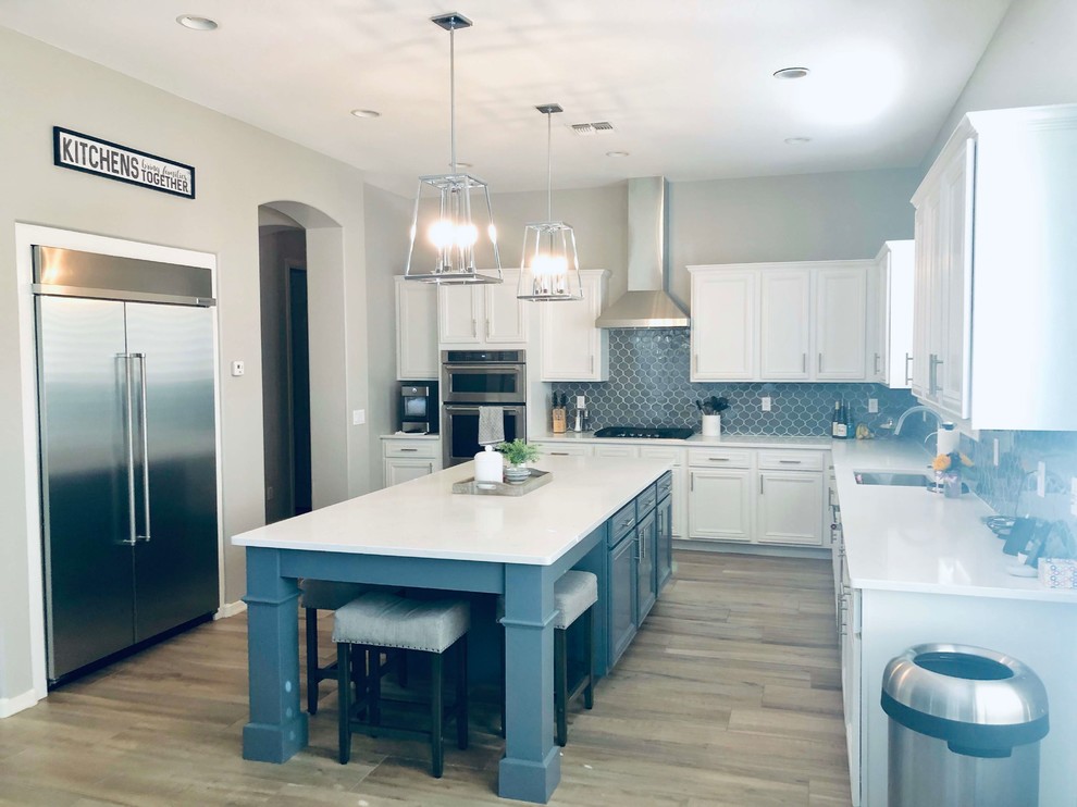 Eat-in kitchen - mid-sized transitional l-shaped porcelain tile eat-in kitchen idea in Phoenix with raised-panel cabinets, quartz countertops, gray backsplash, glass tile backsplash, stainless steel appliances, an island, white countertops, white cabinets and an undermount sink