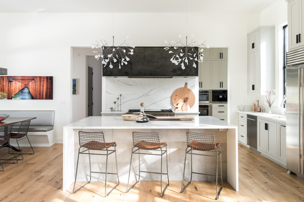 Inspiration for a farmhouse u-shaped kitchen/diner in Austin with shaker cabinets, white cabinets, white splashback, stainless steel appliances, medium hardwood flooring, brown floors and an island.