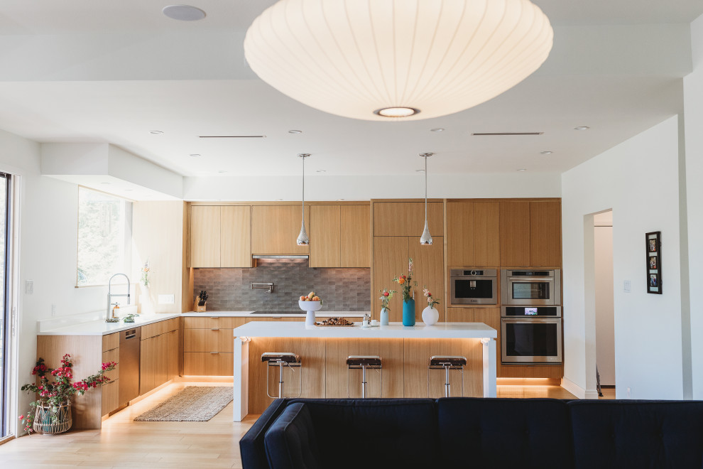 Inspiration for a contemporary l-shaped kitchen in Austin with flat-panel cabinets, medium wood cabinets, grey splashback, stainless steel appliances, light hardwood flooring, an island, beige floors and white worktops.