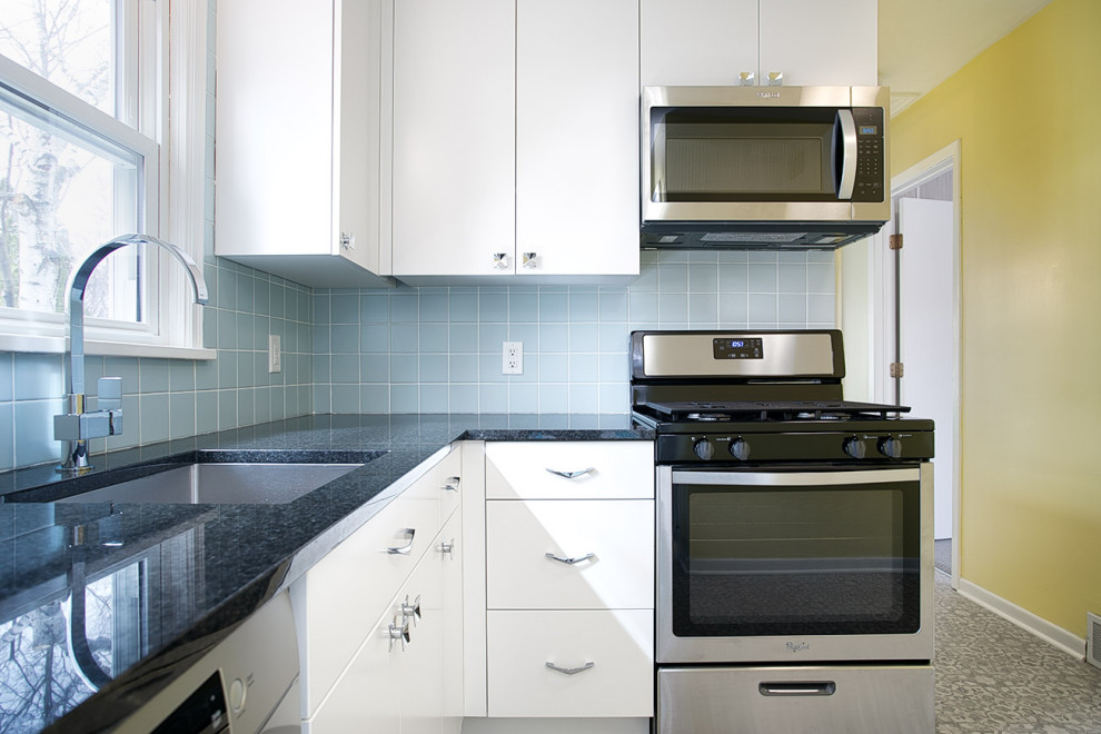Inredning av ett retro avskilt, litet svart svart l-kök, med en undermonterad diskho, släta luckor, vita skåp, granitbänkskiva, blått stänkskydd, stänkskydd i keramik, rostfria vitvaror, vinylgolv och grått golv