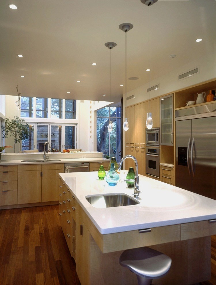 Diseño de cocina contemporánea con electrodomésticos de acero inoxidable, armarios con paneles lisos, puertas de armario de madera clara y encimera de cuarzo compacto