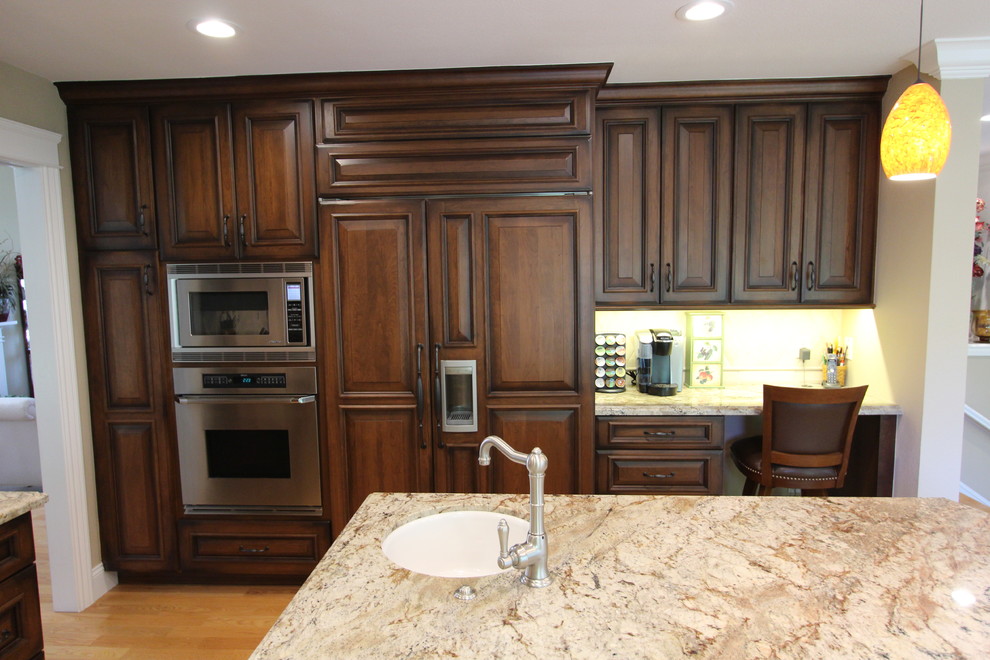 Exempel på ett stort klassiskt kök, med en undermonterad diskho, luckor med upphöjd panel, skåp i mörkt trä, granitbänkskiva, beige stänkskydd, stänkskydd i stenkakel, rostfria vitvaror, mellanmörkt trägolv och en köksö