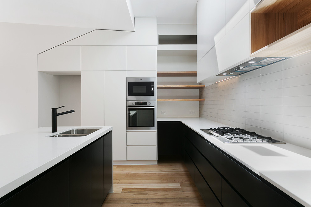 Exempel på ett modernt kök, med vitt stänkskydd, rostfria vitvaror och en köksö