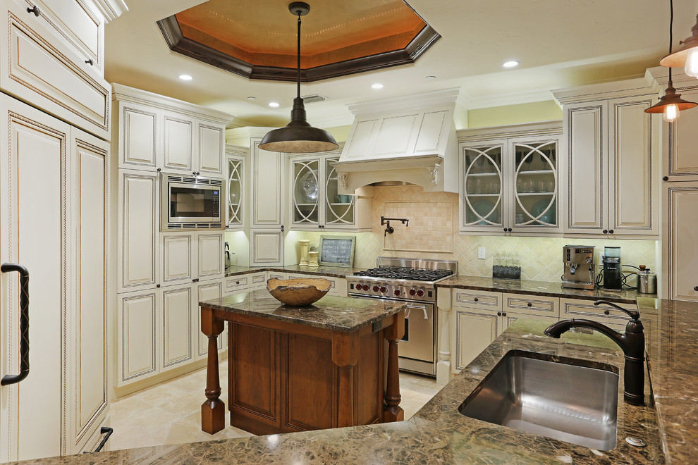 Klassisk inredning av ett mellanstort brun brunt kök, med en enkel diskho, luckor med upphöjd panel, beige skåp, granitbänkskiva, beige stänkskydd, stänkskydd i stenkakel, integrerade vitvaror, travertin golv, en halv köksö och beiget golv