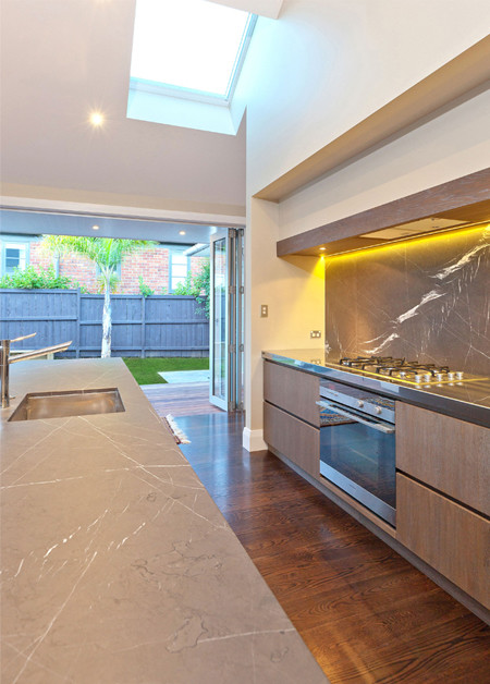 Eat-in kitchen - mid-sized contemporary single-wall medium tone wood floor and brown floor eat-in kitchen idea in Auckland with an undermount sink, flat-panel cabinets, medium tone wood cabinets, marble countertops, gray backsplash, marble backsplash, stainless steel appliances and an island