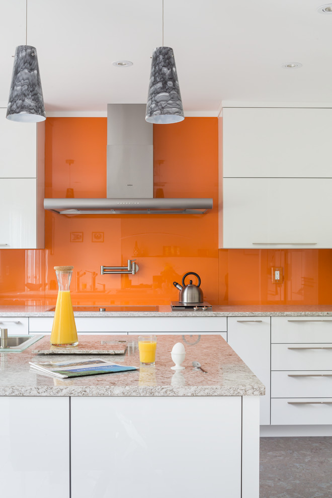 Bild på ett mellanstort funkis kök och matrum, med en dubbel diskho, släta luckor, vita skåp, bänkskiva i kvarts, orange stänkskydd, glaspanel som stänkskydd, rostfria vitvaror och en halv köksö