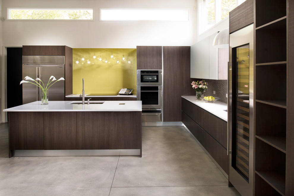 Esempio di una cucina minimalista di medie dimensioni con lavello sottopiano, ante lisce, ante in legno bruno, paraspruzzi giallo, elettrodomestici in acciaio inossidabile e pavimento in cemento