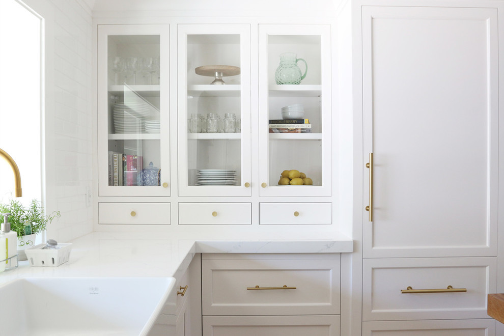 Cette image montre une arrière-cuisine avec des portes de placard blanches, plan de travail en marbre, une crédence blanche, parquet clair et îlot.