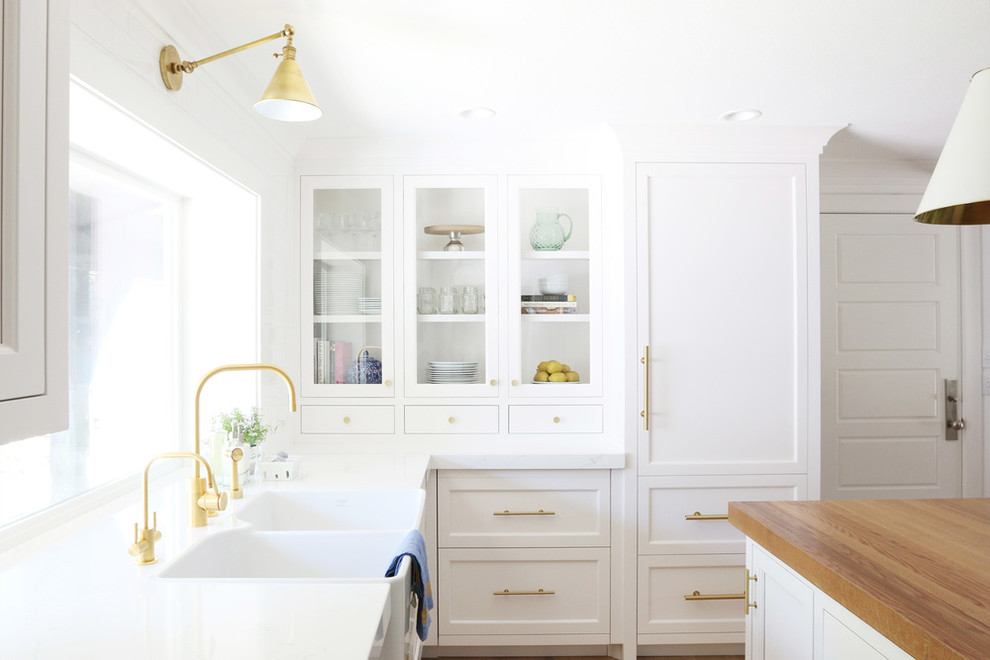 This is an example of a kitchen pantry in Salt Lake City with white cabinets, marble worktops, white splashback, light hardwood flooring and an island.