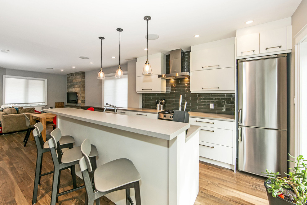 This is an example of a medium sized contemporary galley kitchen/diner in Toronto with a double-bowl sink, flat-panel cabinets, white cabinets, engineered stone countertops, grey splashback, ceramic splashback, stainless steel appliances, medium hardwood flooring and an island.