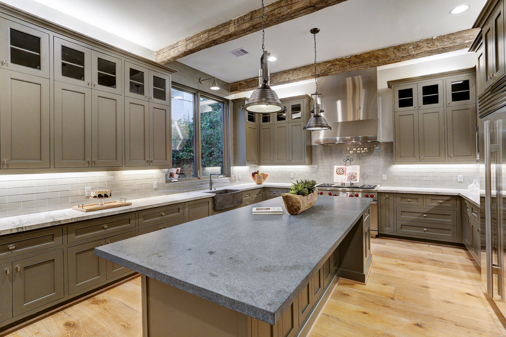 Example of a mid-sized transitional u-shaped light wood floor and beige floor open concept kitchen design in Houston with a farmhouse sink, recessed-panel cabinets, gray cabinets, quartzite countertops, gray backsplash, subway tile backsplash, stainless steel appliances, an island and gray countertops