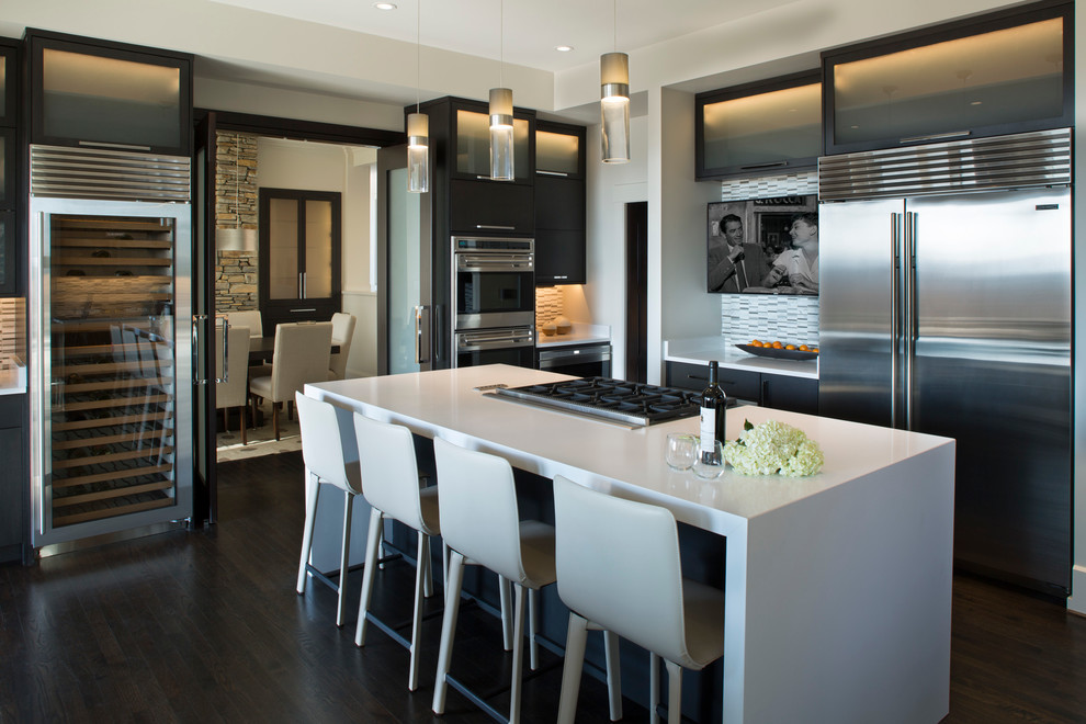 Inspiration for a large modern dark wood floor enclosed kitchen remodel in Other with a double-bowl sink, glass-front cabinets, dark wood cabinets, solid surface countertops, multicolored backsplash, stone tile backsplash, stainless steel appliances and an island