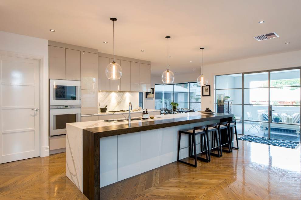 Immagine di una cucina design con lavello sottopiano, ante lisce, ante grigie, paraspruzzi grigio e pavimento in legno massello medio