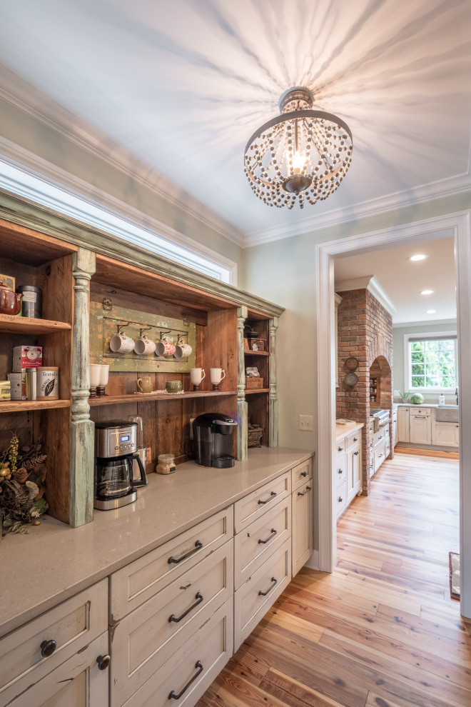 Large farmhouse u-shaped kitchen pantry in Detroit with recessed-panel cabinets, distressed cabinets, engineered stone countertops, stainless steel appliances, light hardwood flooring, an island and white worktops.