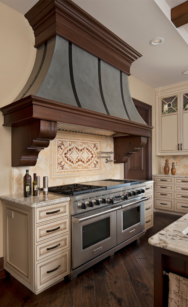 Klassisk inredning av ett kök, med beige skåp, beige stänkskydd, rostfria vitvaror och mörkt trägolv